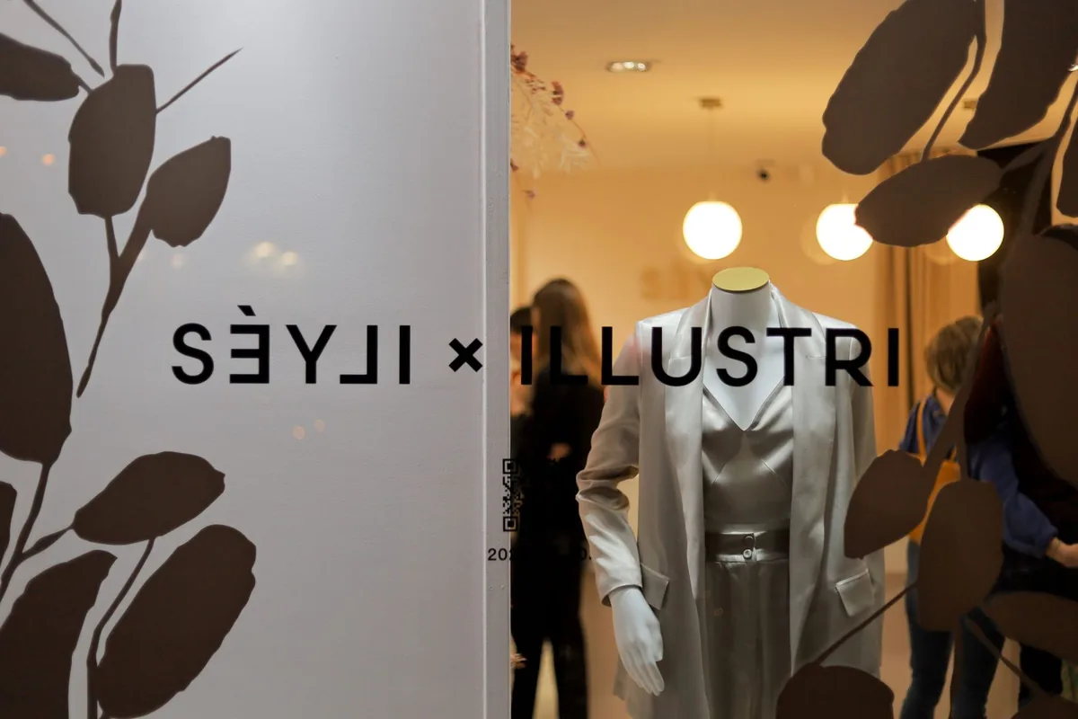 A SÉYLI x Illustri kiállítás felirata és egy fehér összeállítás a Boutique kirakatában